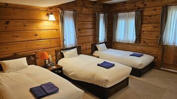 A room with three beds, wooden walls, and a nightstand with a lamp.
