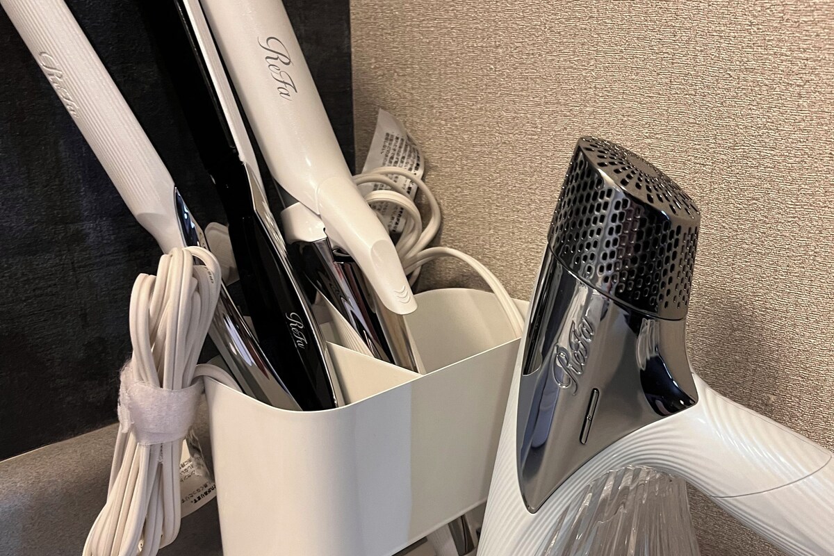 A white charging station with a hairdryer, a vacuum cleaner, and a metal appliance.