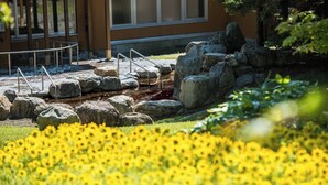 A garden with yellow flowers, rocks, and a building with large windows. - Yunni no Yu (Yuni)