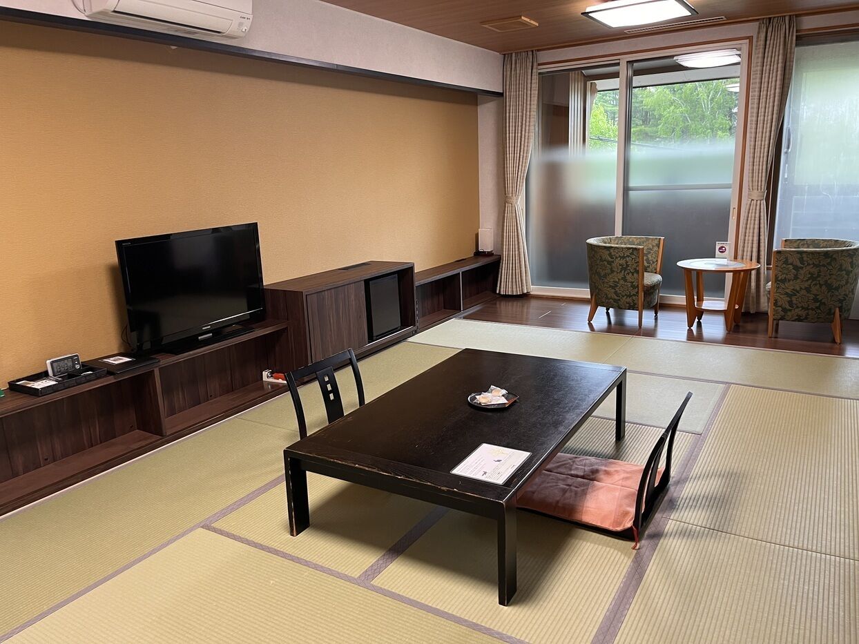 Una habitación con suelo de tatami, televisión, una mesa con mantel individual y sillas.