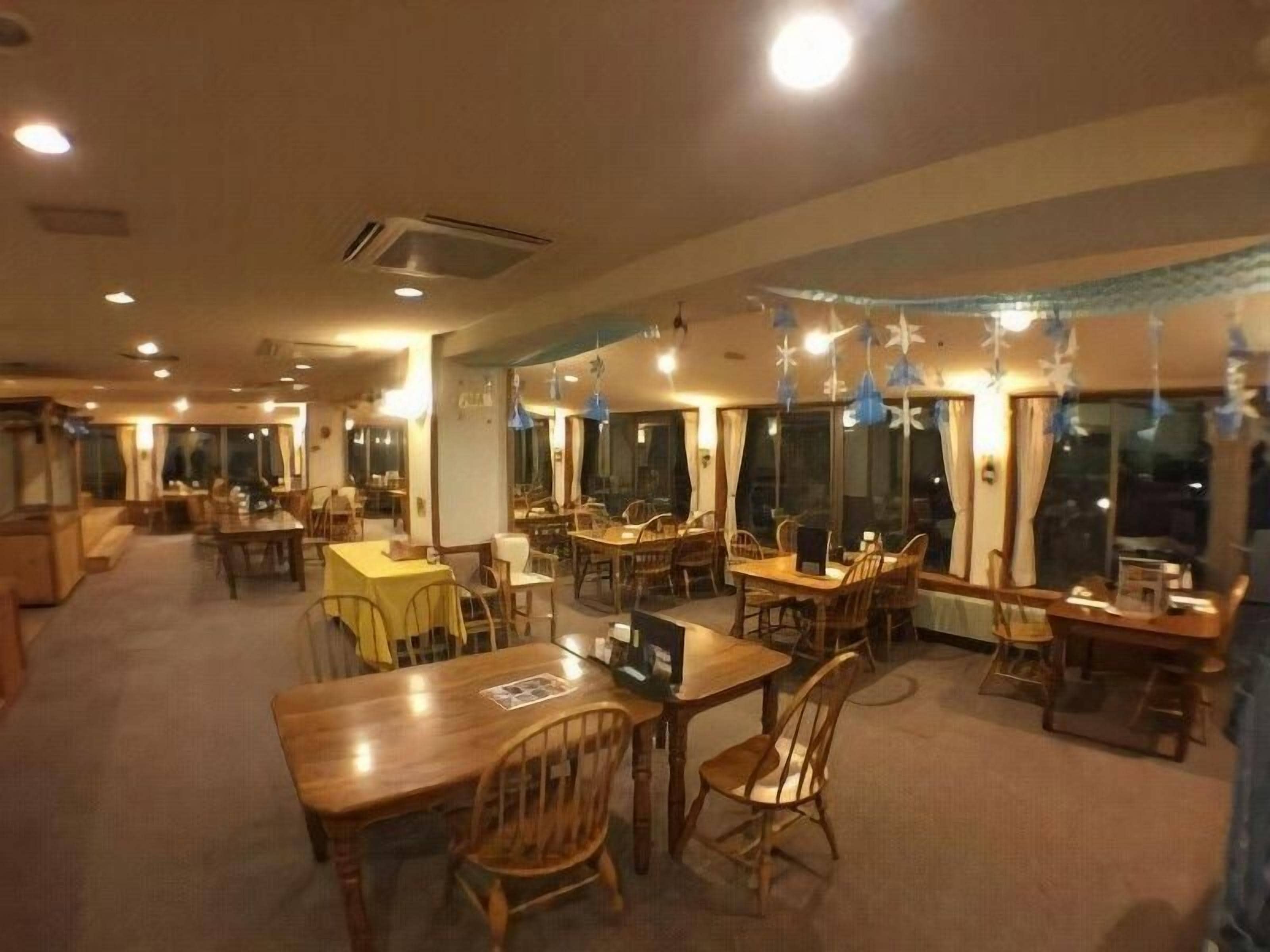 A restaurant with multiple dining tables and chairs, large windows, and hanging decorations.