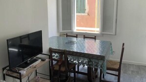 A dining area with a table, chairs, a TV, and a window with shutters. - Bright apartment downtown La Ciotat - 2 min from the port (La Ciotat)