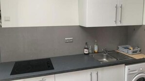 A kitchen with a black induction cooktop, a sink, and a washing machine. - Bright apartment downtown La Ciotat - 2 min from the port (La Ciotat)