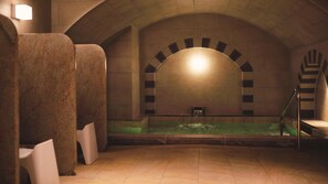 Ein Wellnessbereich mit einer großen Badewanne, einer Sitzbank und einer Wand mit einem einzigartigen Bogenmuster.