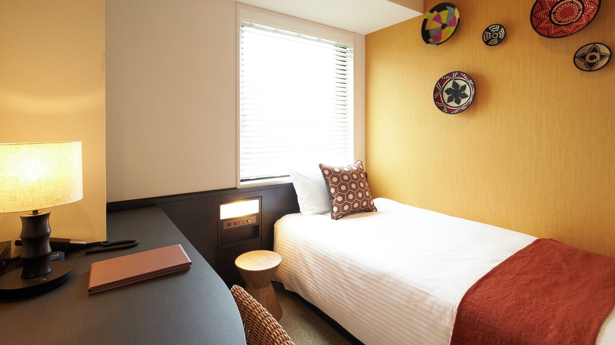 A hotel room with a bed, desk, lamp, chair, and wall decorations.