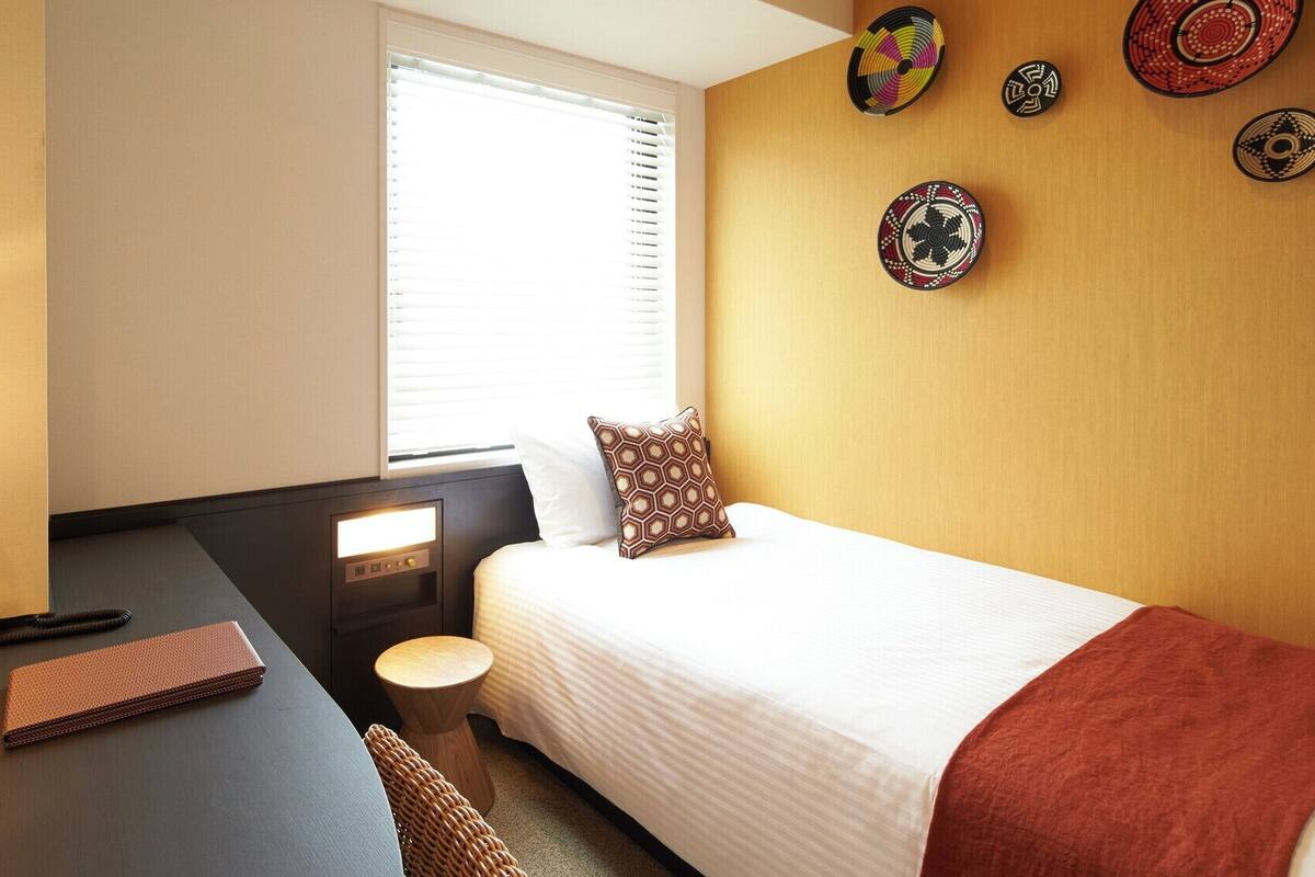 A hotel room with a bed, desk, lamp, chair, and wall decorations.