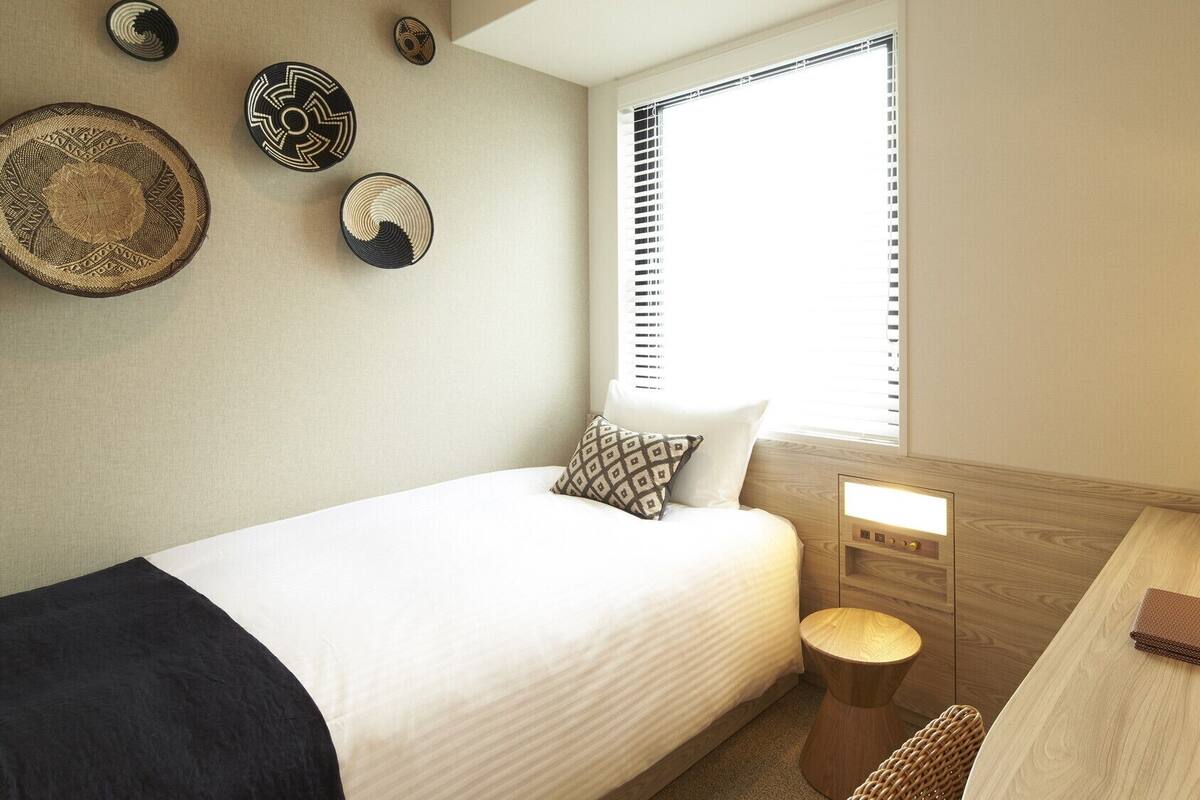 A hotel room with a bed, bedside table, lamp, and decorative wall art.
