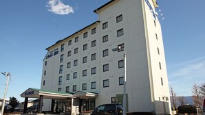 Ein mehrstöckiges Hotel mit schlichter Fassade, einem überdachten Eingang und einem geparkten Auto davor.