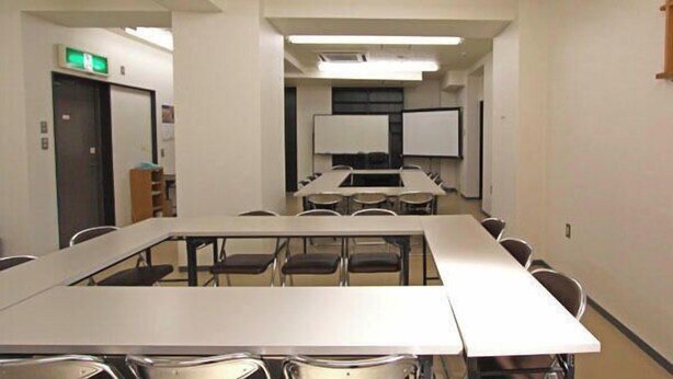 Ein Konferenzraum mit langem Tisch, Stühlen, einer Whiteboard und einer Projektionsleinwand.