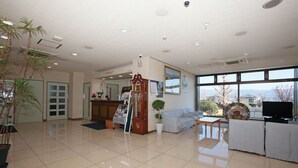 Eine Hotelhalle mit einer Rezeption, einer Uhr, einem Sofa, einem Fernseher und einem großen Fenster mit Blick auf die Berge.