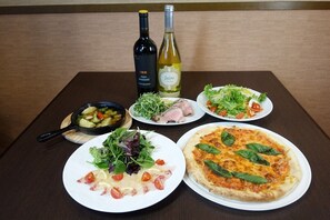 Una mesa con platos de comida, un tazón de ensalada y dos botellas de vino.
