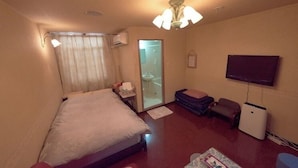 A hotel room with a bed, a television, a small table, a sofa, and a sliding door leading to a bathroom. - Hotel 4F Macaroni (Osaka)