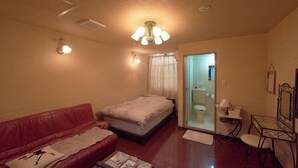 A bedroom with a bed, a red leather sofa, a small table, a mirror, and a bathroom with a toilet and sink. - Hotel 4F Macaroni (Osaka)