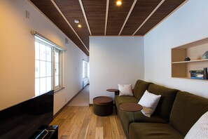A modern living room with a wooden floor, a green sofa, a flat-screen TV, and a small bookshelf.