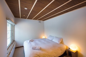 A bedroom with a large bed, bedside lamps, a window, and a wooden ceiling.