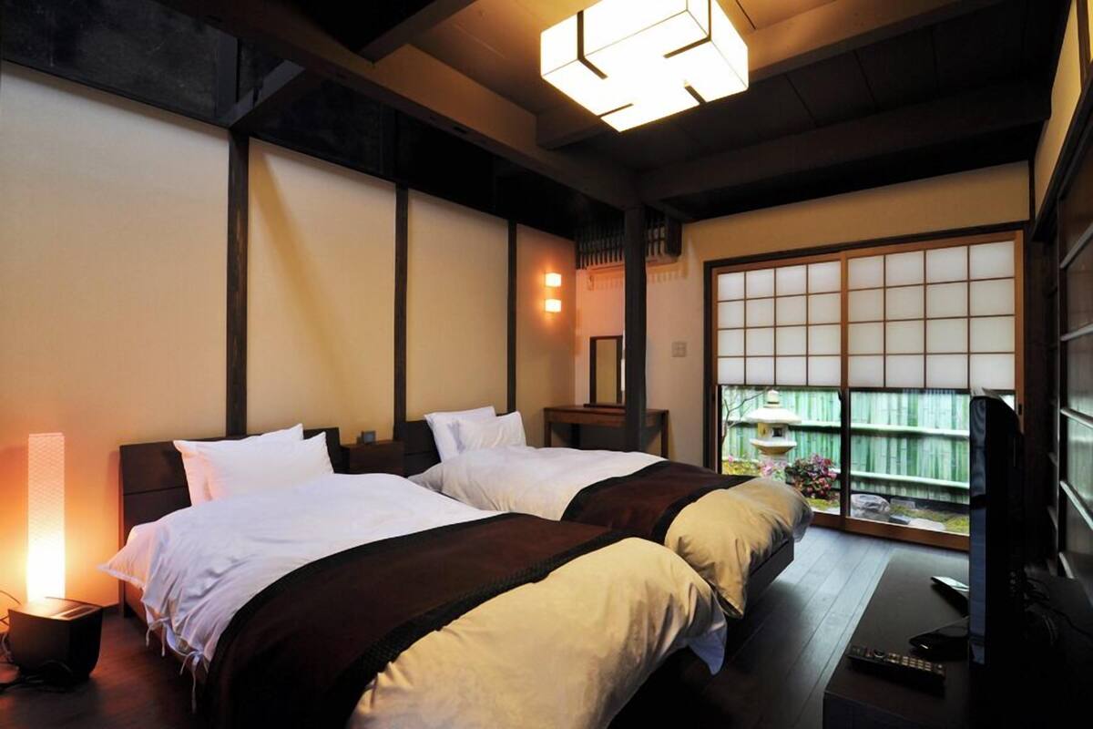 A traditional Japanese-style room with tatami flooring, a low wooden bed, a shoji screen, and a television.
