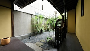 A traditional Japanese interior with tatami flooring, a low wooden ceiling, and a view of a garden with bamboo and a stone lantern. - Kuraya Senbonsanjo (Kyoto)