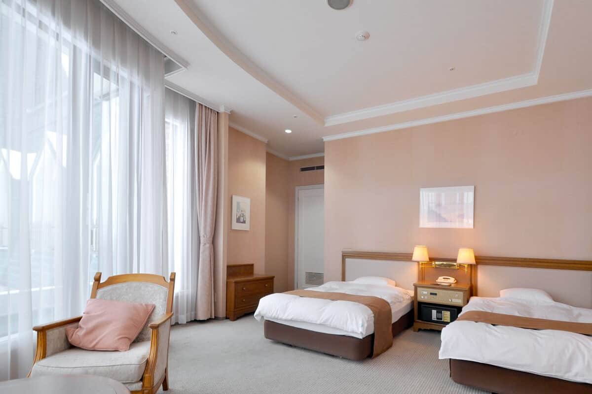 A hotel room with two beds, a chair, a table, and a window with curtains.