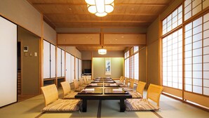 Een traditionele Japanse kamer met tatami vloeren, een lage tafel met kussens, schuifdeuren en een hanglamp.