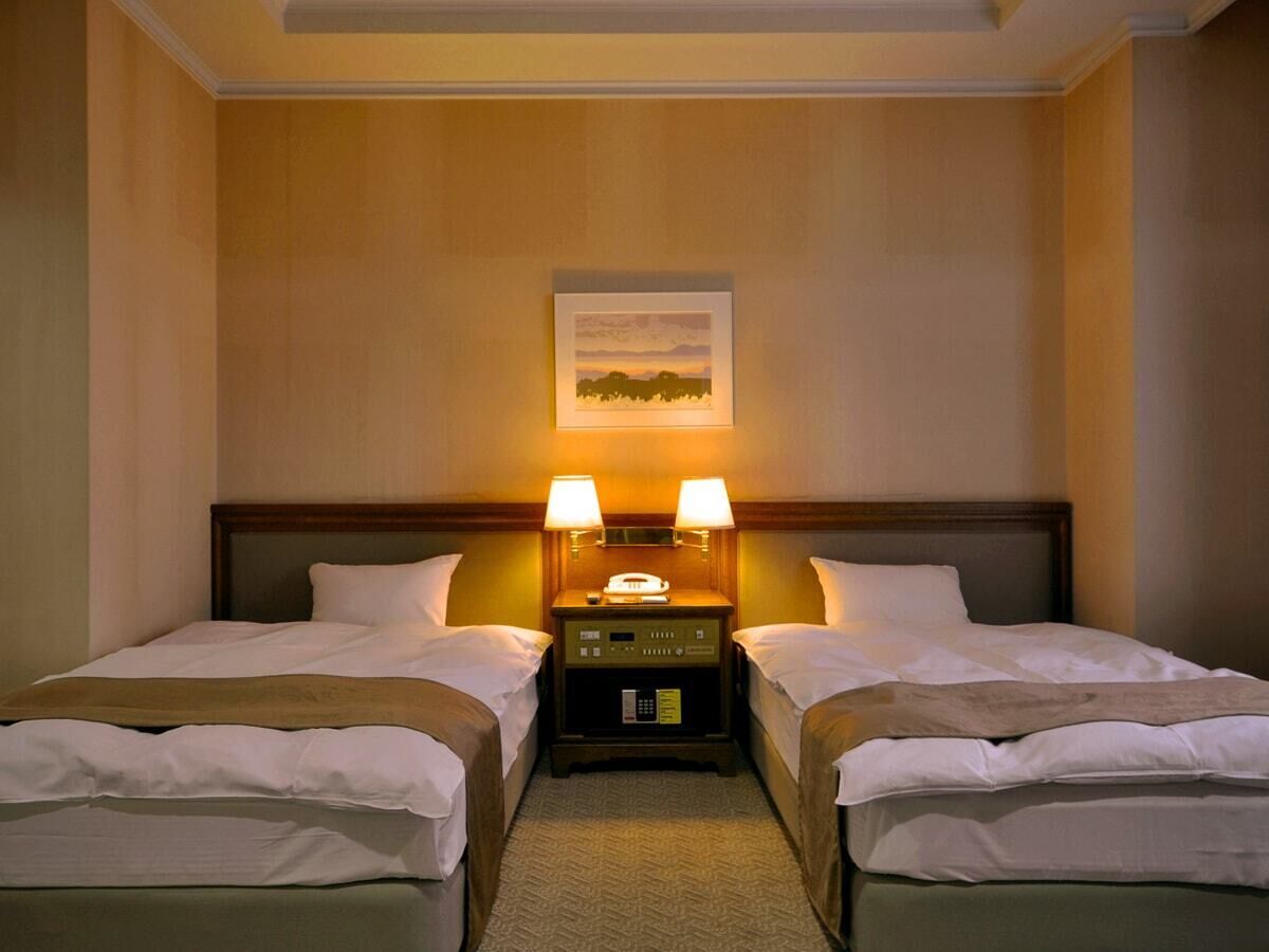 A hotel room with two beds, a nightstand with lamps, a painting on the wall, and a carpeted floor.