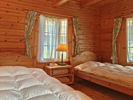Habitación de cabaña de madera con dos camas, una mesita de noche con lámpara y cortinas en las ventanas.