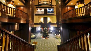 Een statige lobby met een kerstboom in het midden, meerdere verdiepingen en een klassieke houten trap.