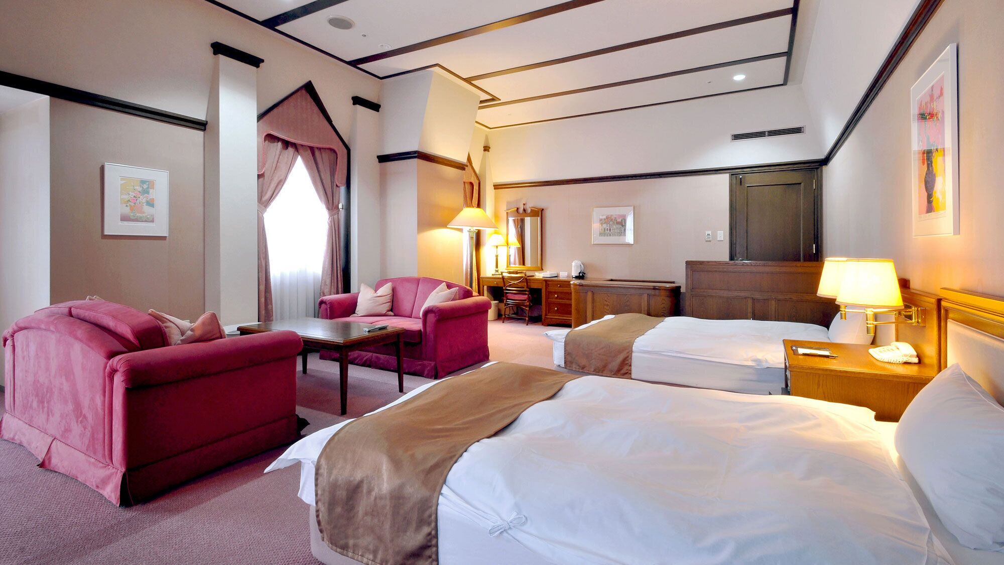 A hotel room with two beds, a desk, a chair, and a sofa.
