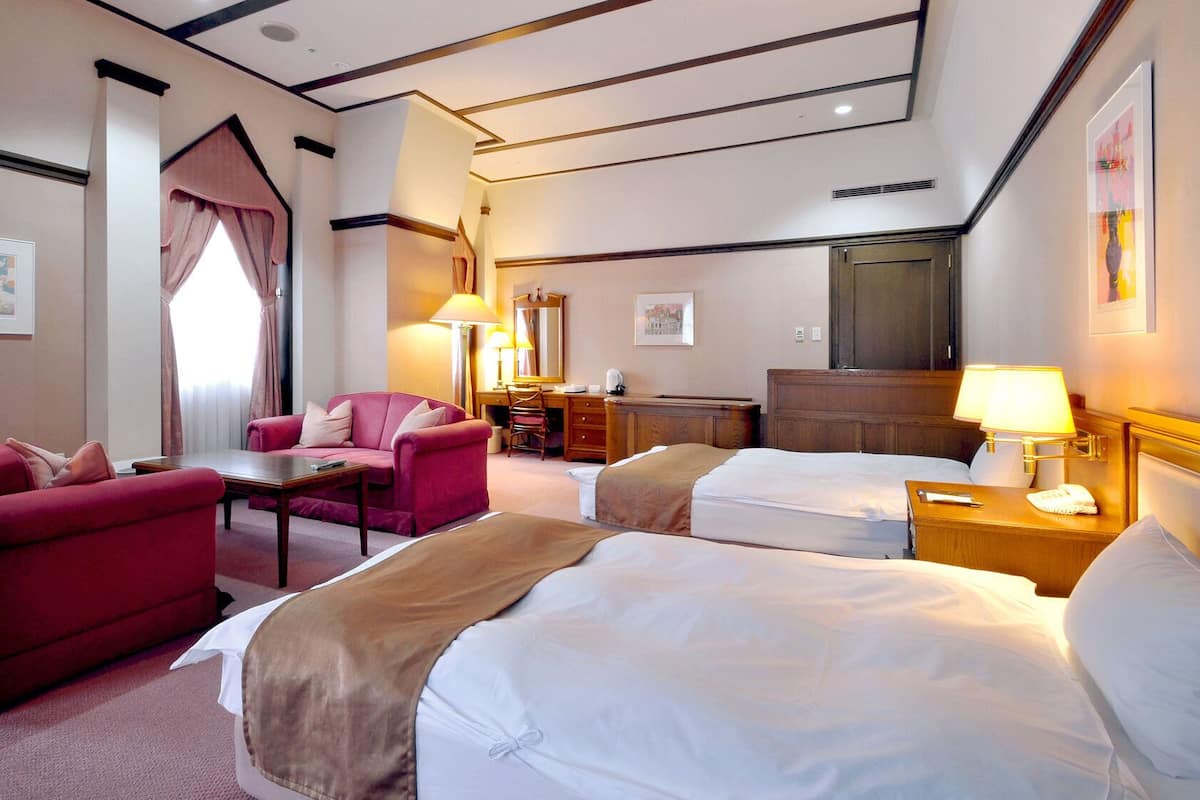 A hotel room with two beds, a desk, a chair, and a sofa.