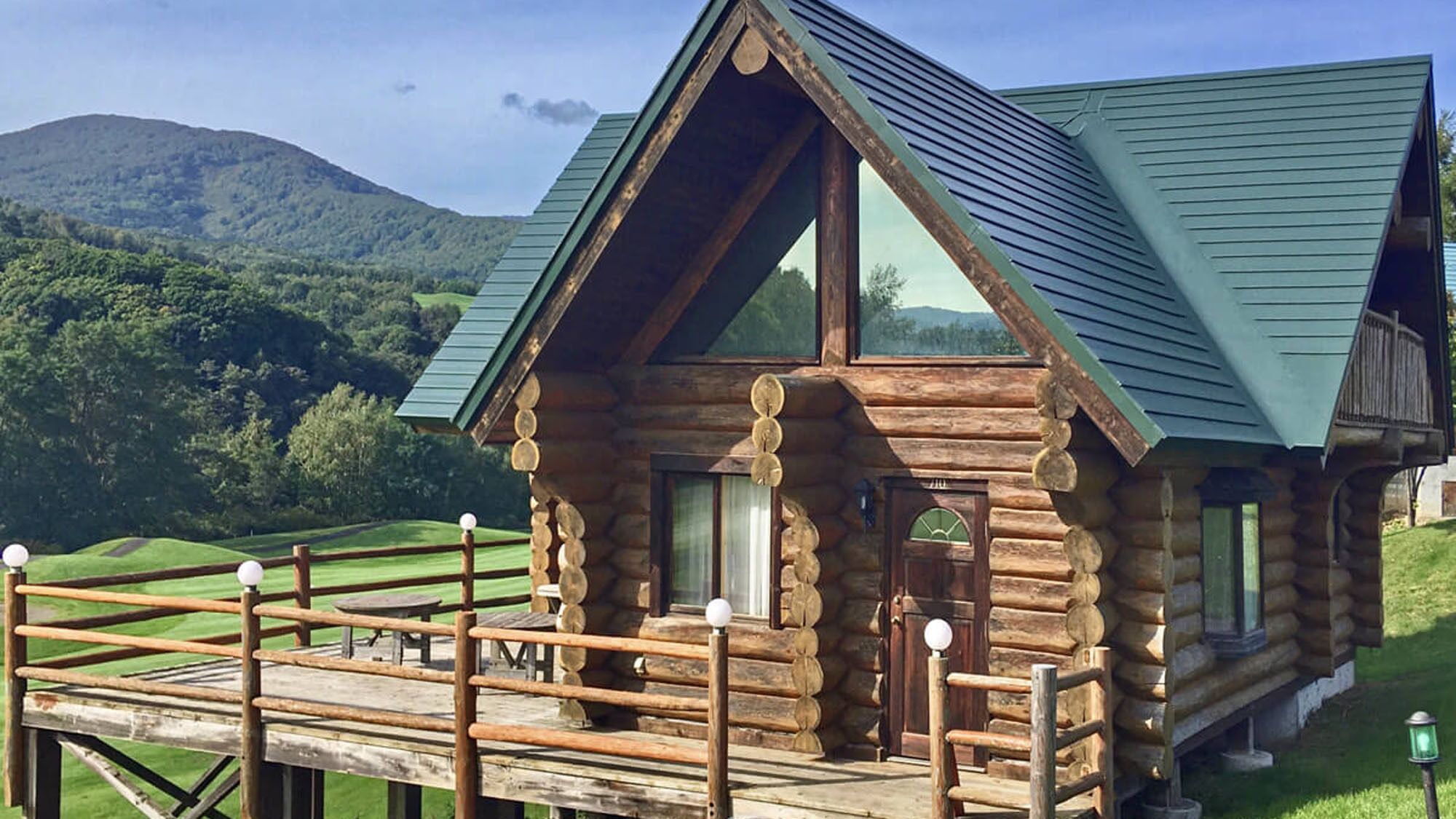 A log cabin with a balcony, large windows, and a green roof.