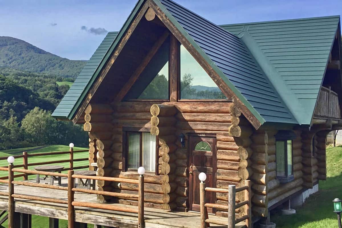 A log cabin with a balcony, large windows, and a green roof.