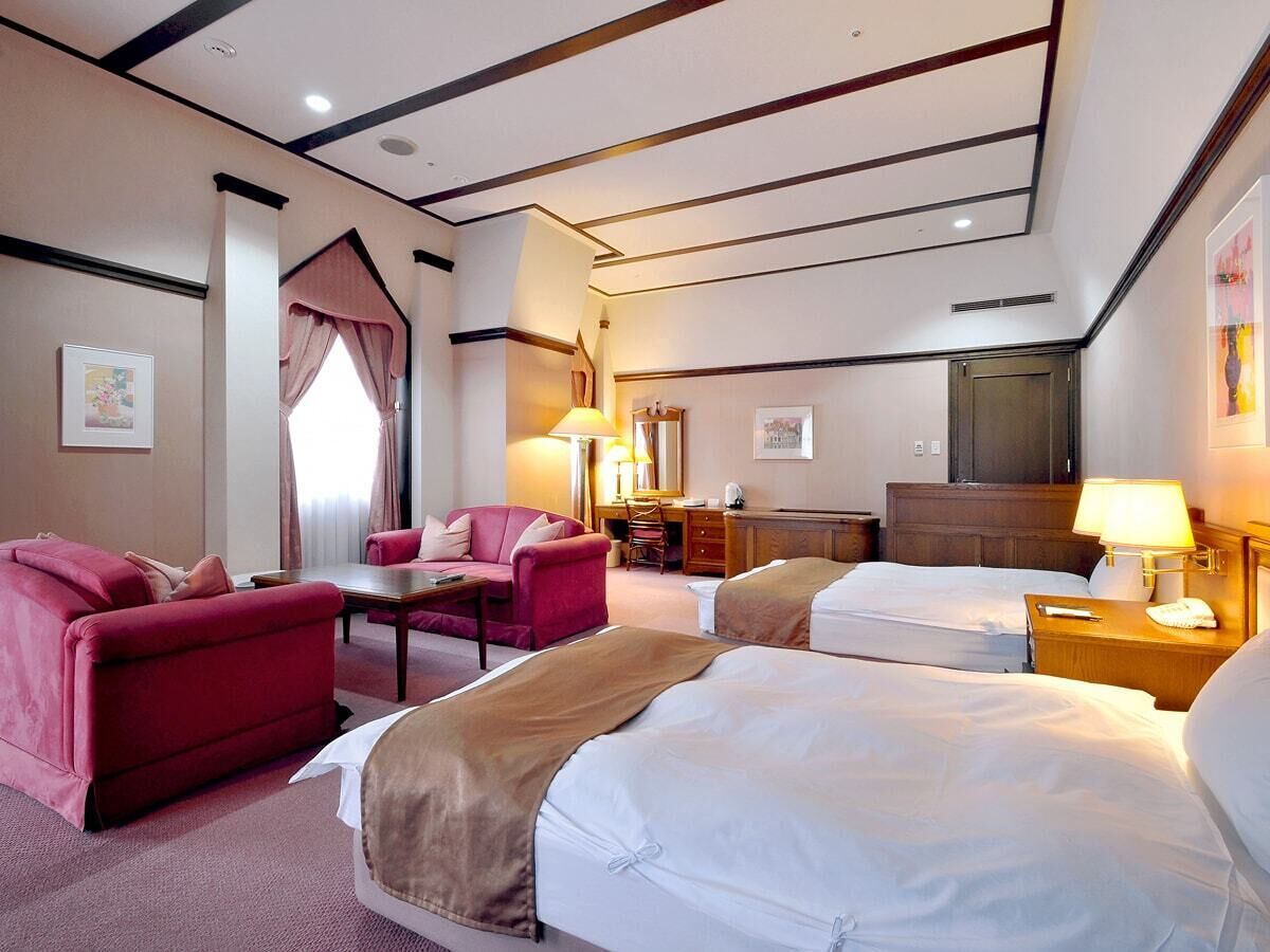 A hotel room with a bed, a desk, a chair, a sofa, and a television.