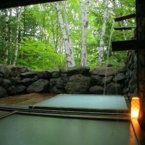 A room with a tatami mat, a stone wall, and a view of a forest.
