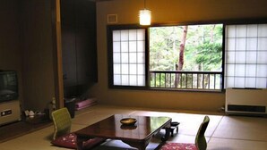 A tatami mat room with a low table, chairs, a television, and a view of greenery outside. - Shibu Tatsunokan (Chino)