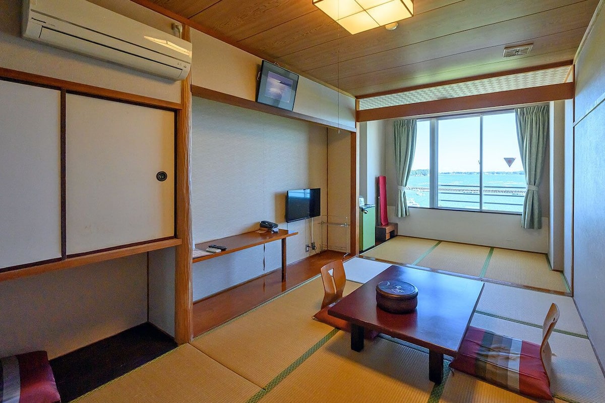 Habitació japonesa tradicional amb tatami, televisió, taula petita i finestra amb cortines.
