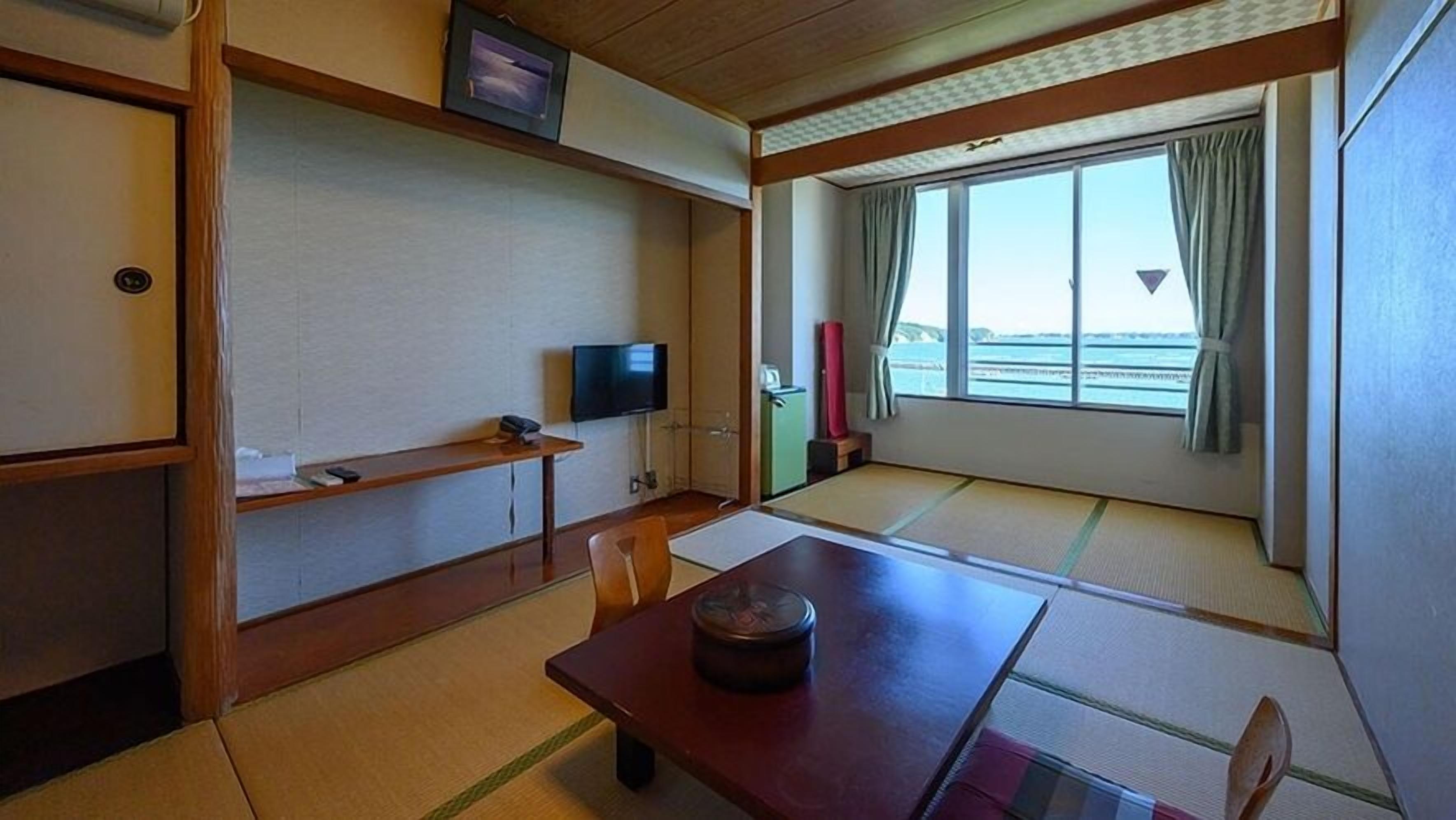 Quarto com piso de tatame, televisão, uma pequena mesa e janela com vista.