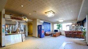 A hotel lobby with a reception desk, vending machine, seating area, and a bar. - Amigen (Toba)