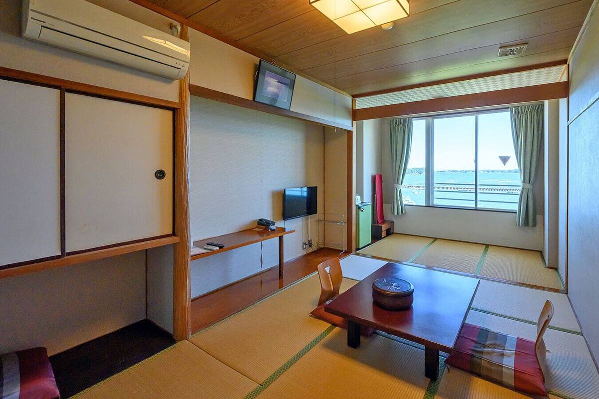Habitació japonesa tradicional amb tatami, televisió, taula petita i objecte decoratiu, i finestra amb cortines.