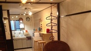 Ett rum med ett matbord, en flätstol, en liten pall, ett runt bord och en hängande lampa.