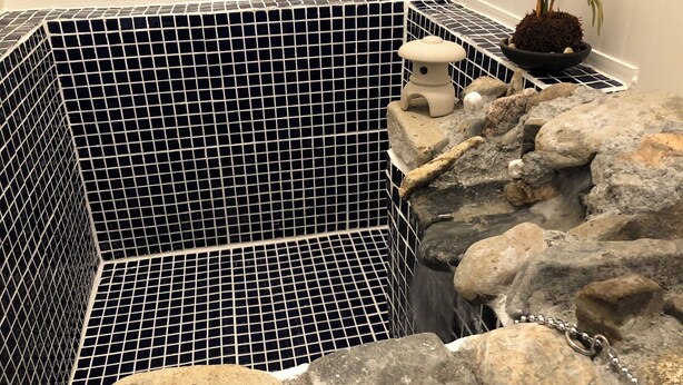 En pool med kakelbeklädd botten, en stenformation och en liten vit lykta.