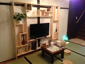 A living room with a TV, wooden shelves, a coffee table, and a tatami mat floor. - Kyoto Higashiyama Kurumi (Kyoto)