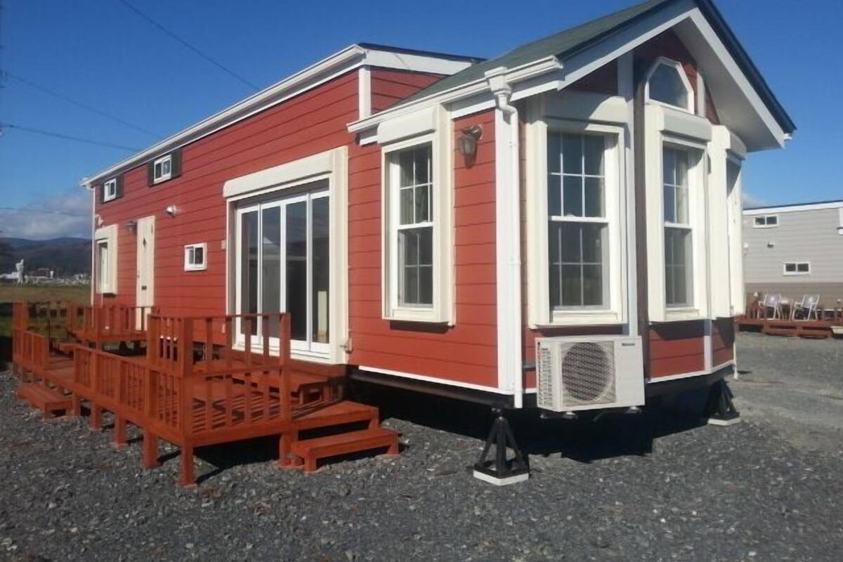 A red building with white trim, large windows, and a small porch with wooden chairs.