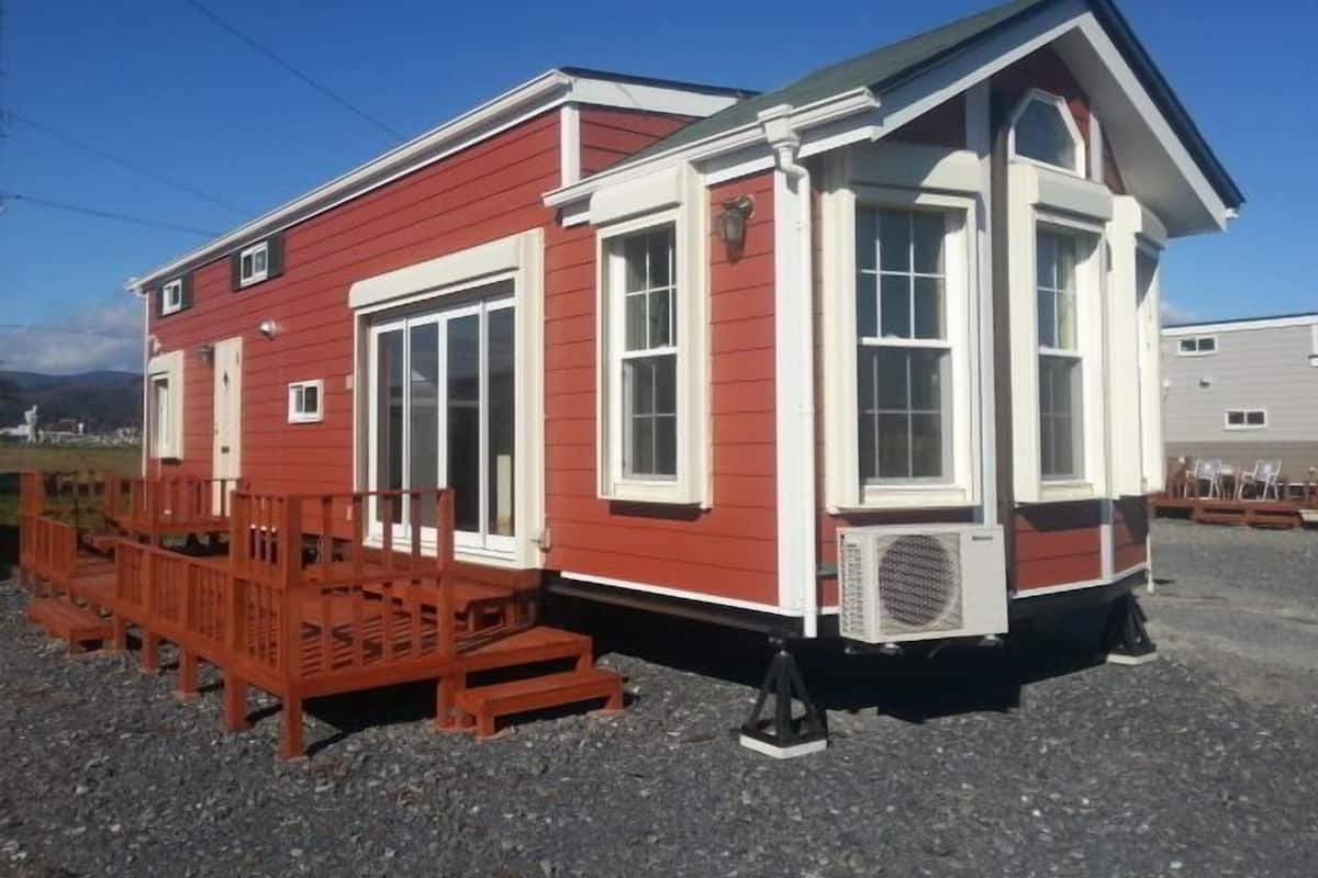 Un bâtiment rouge avec des ornements blancs, de grandes fenêtres et un petit porche doté de chaises en bois.