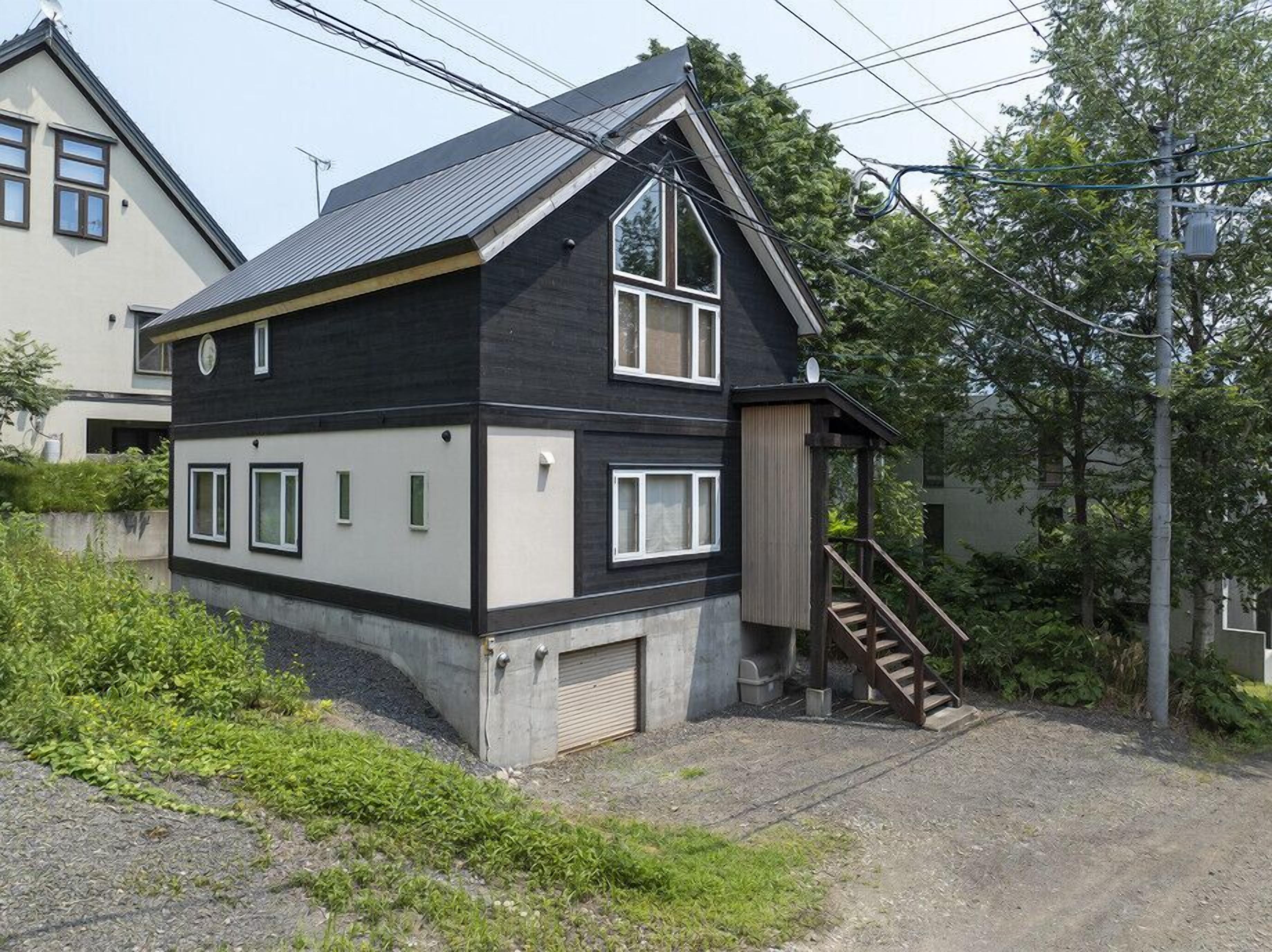 A two-story house with a steep gable roof, a front porch with a staircase, and a garage door.