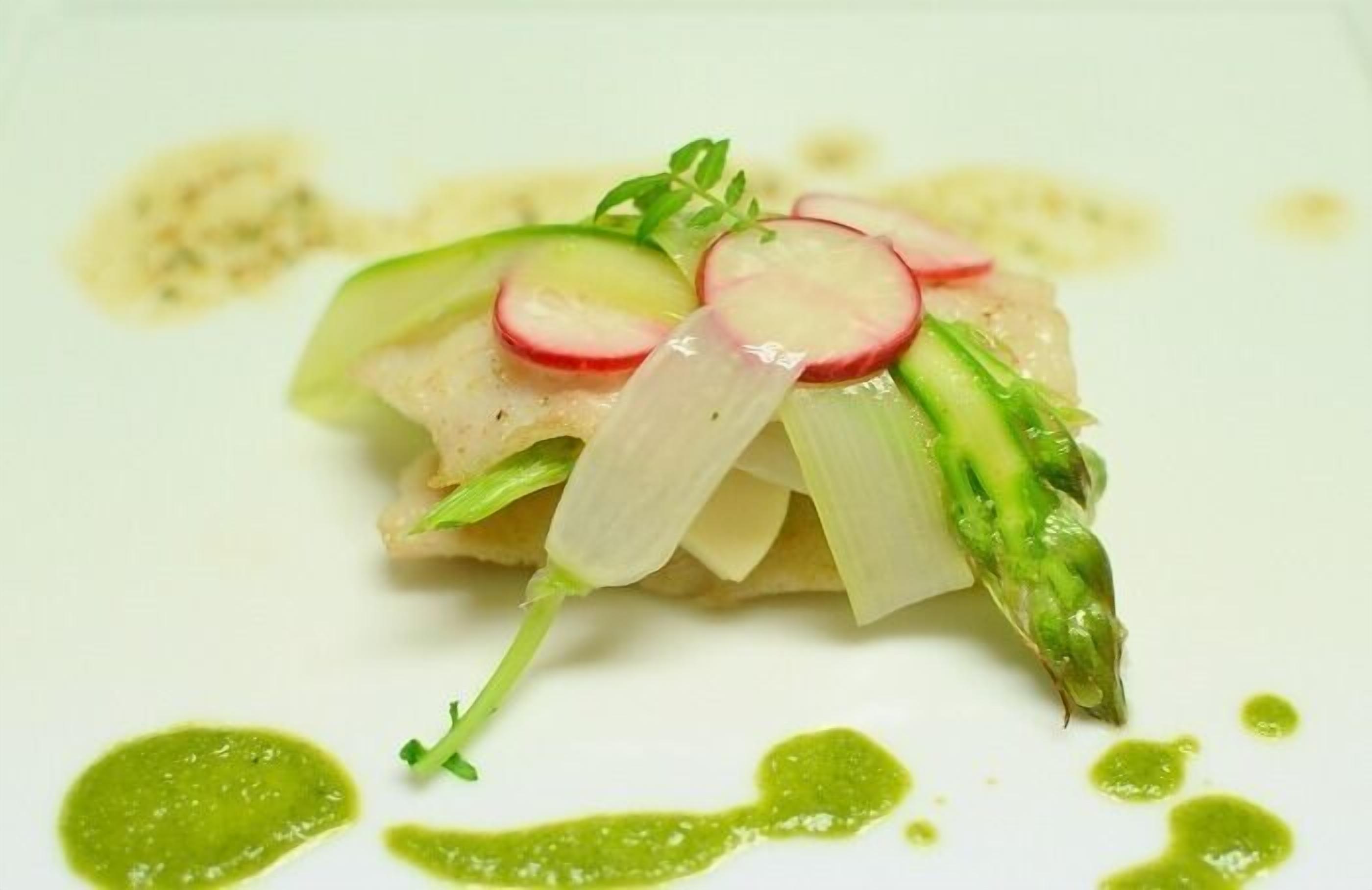 A dish with a white plate, green sauce, and a garnish of radish and asparagus.