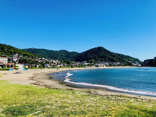 Une ville côtière avec une plage, un ciel bleu azur et des collines verdoyantes en arrière-plan.
