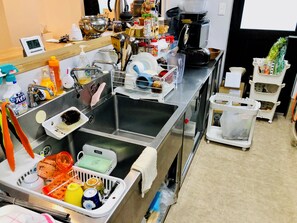 Une cuisine équipée d’un évier en acier inoxydable, de divers ustensiles de cuisine, d’une machine à café et de paniers de rangement.