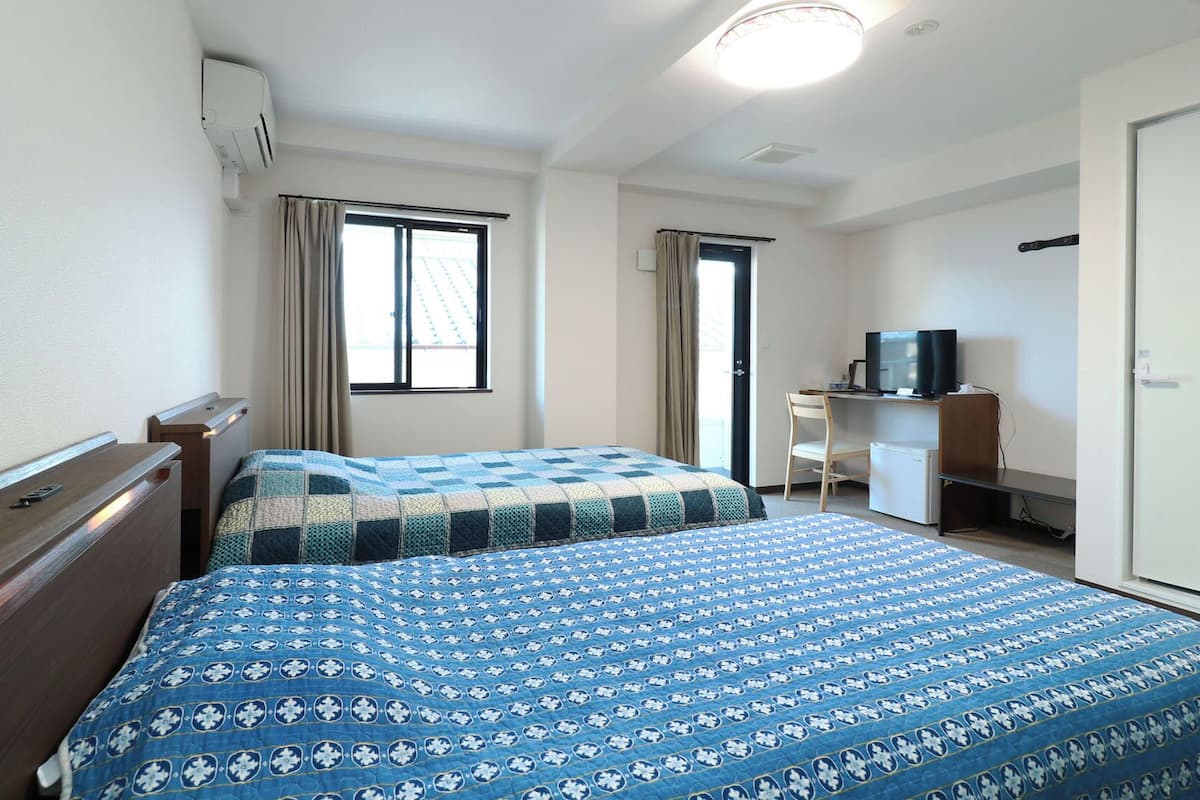 Una habitación de hotel con dos camas, un escritorio con televisor y un armario.