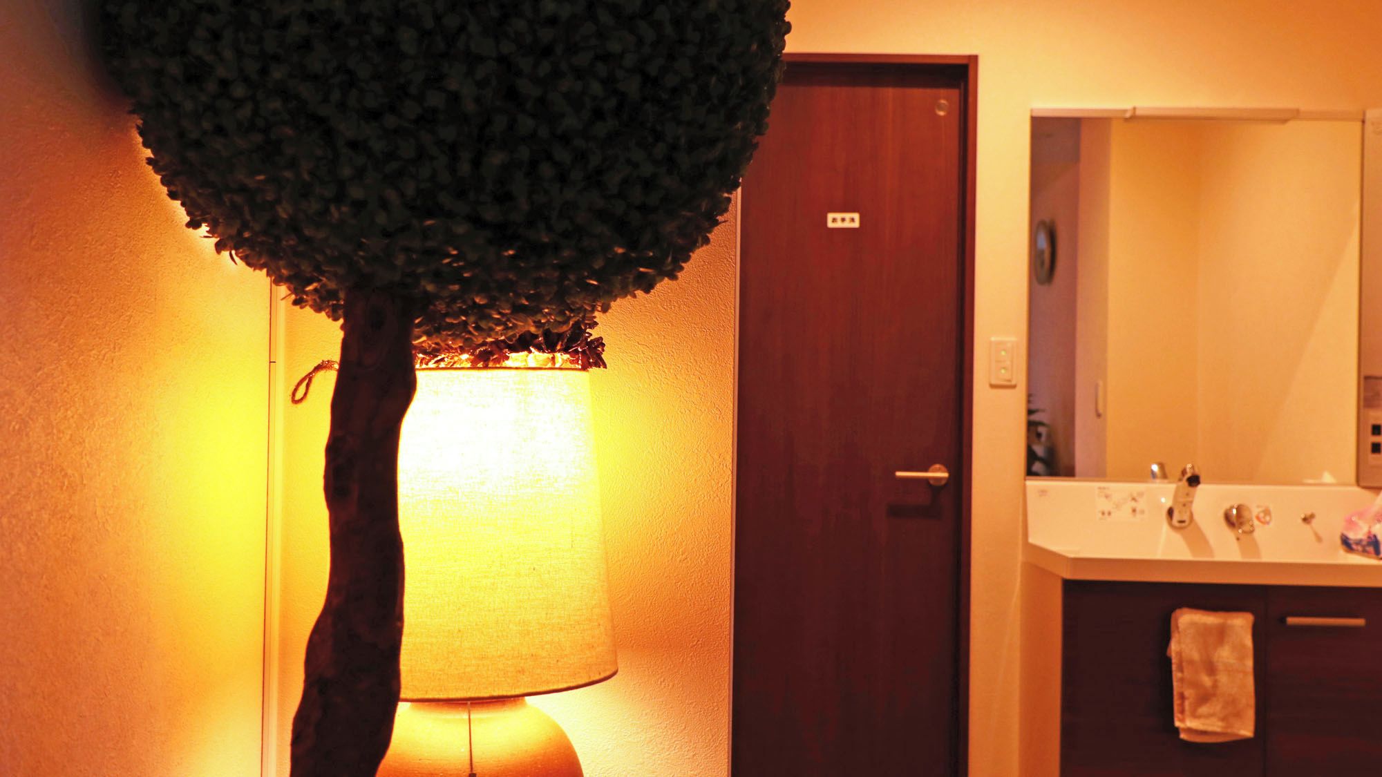 A bathroom with a tree-shaped lamp, a wooden door, and a mirror.