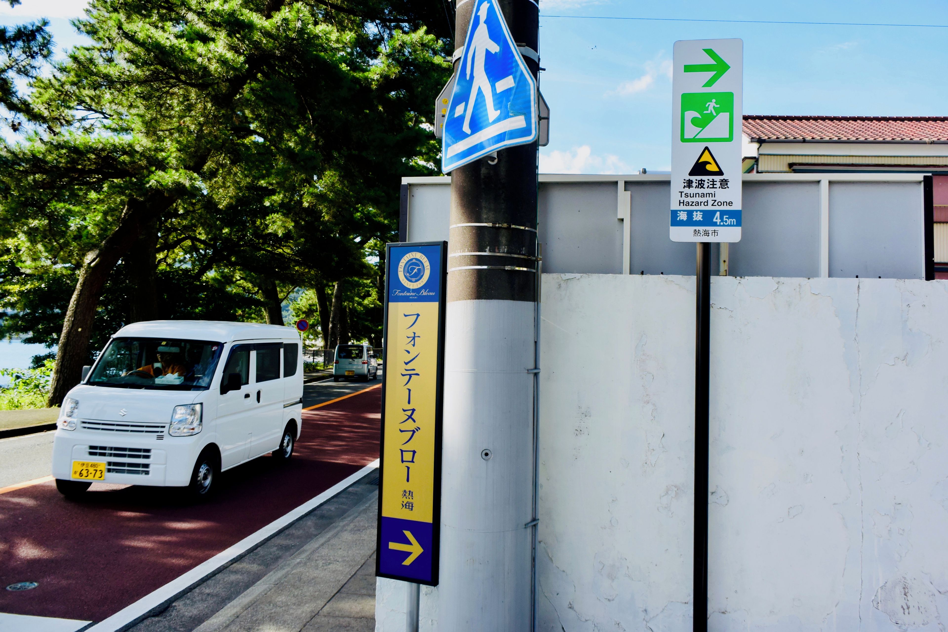 A white van parked on a road with a pedestrian crossing sign and a tsunami hazard zone sign.