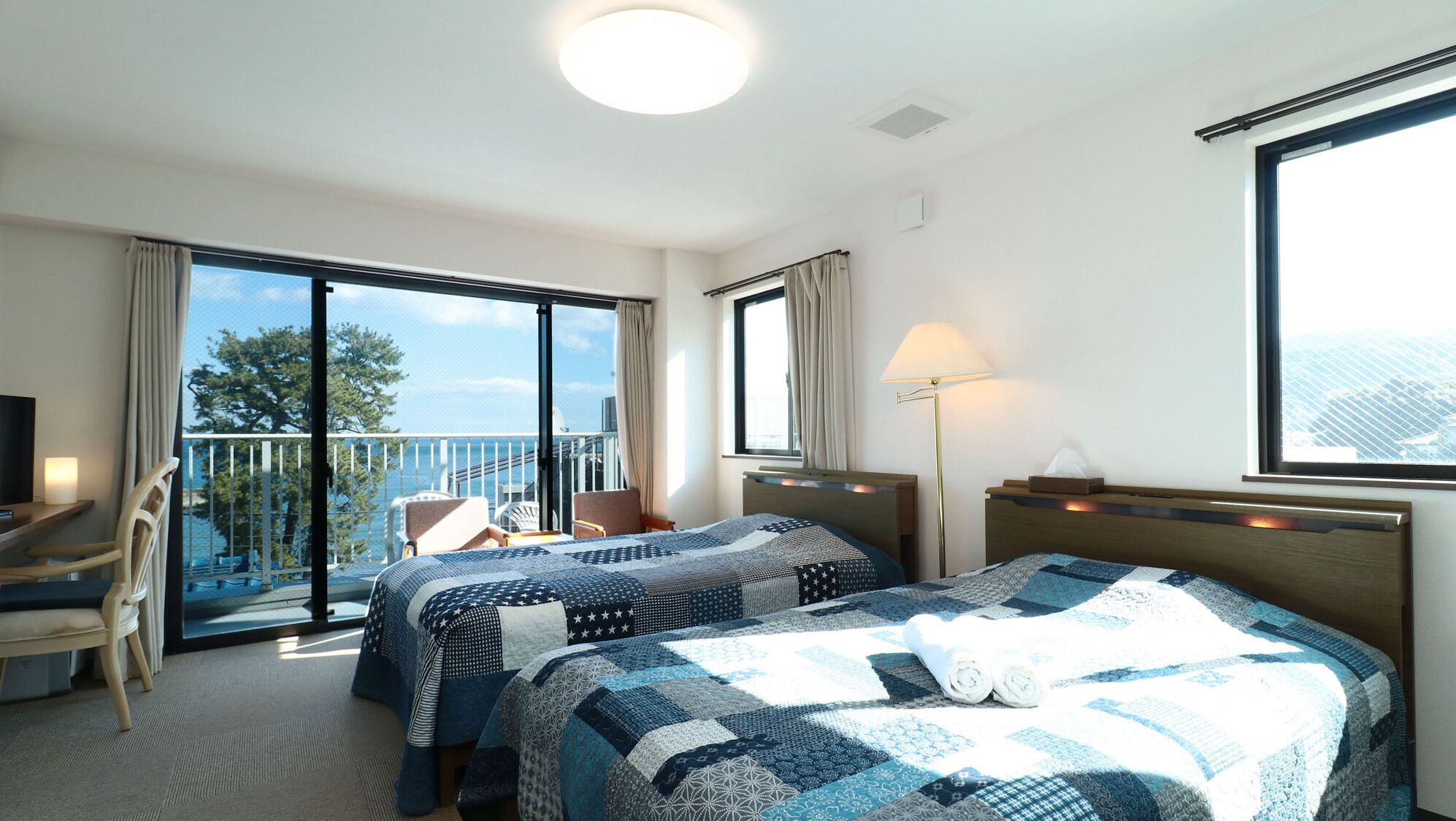 Habitación de hotel con dos camas, un balcón con vistas, un escritorio y una silla.